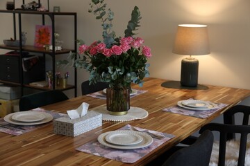 Beautiful table setting with bouquet and napkins indoors. Roses and eucalyptus branches in vase