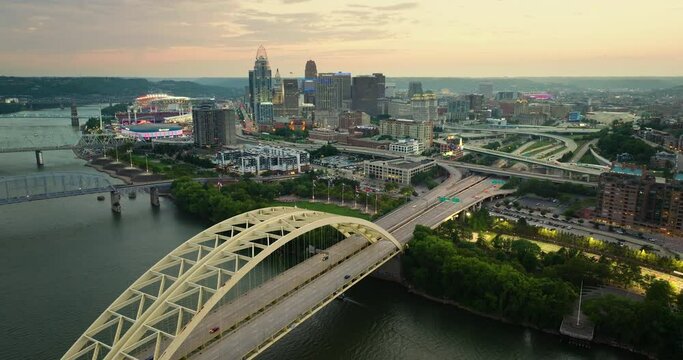 Driving cars on Daniel Carter Beard Bridge highway near illuminated high skyscraper buildings in downtown district of Cincinnati, Ohio, USA. American city with business financial district at sunset