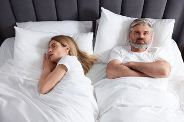 Irritated man lying near his snoring wife in bed at home