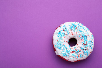 Sweet glazed donut decorated with sprinkles on purple background, top view and space for text. Tasty confectionery