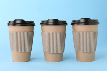 Paper cups with black lids on light blue background. Coffee to go