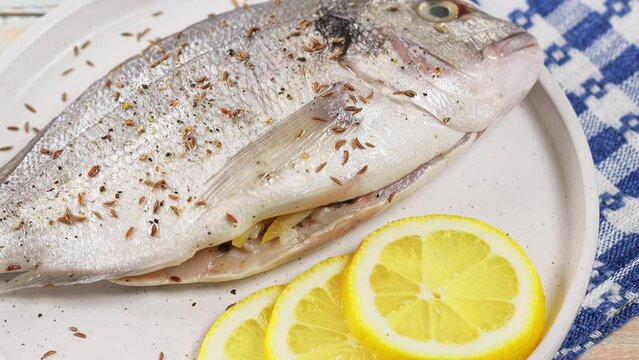 Raw dorado fish with lemon and sprinkled with cumin on white plate. Handheld shot