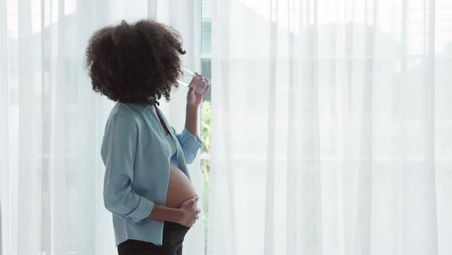 Woman tenderly caressing baby bump while sipping water