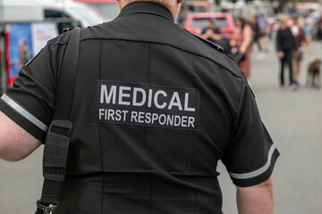 A medical first responder wearing a black and white reflective uniform with the words medical first...