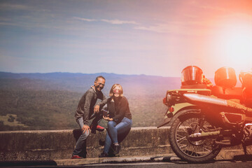couples of biker toothy smiling with happiness beside small motorcycle at traveling destination