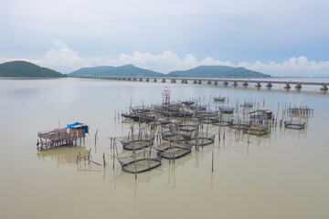 Fototapeta premium Aerial view of fishing trap net in canel with fisherman urban city village town houses, lake or river. Nature landscape fisheries and fishing tools at Pak Pha, Songkhla, Thailand. Aquaculture farming