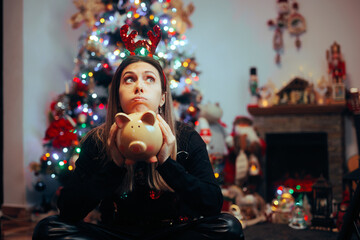 Broke Woman Holding a Piggy Bank Regretting Christmas Spendings. Desperate girl feeling sad about...