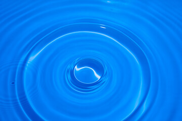 A droplet of water dispersing on a blue surface, alongside empty space for adding text.