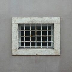 old window on stone frame with bars against rendered wall