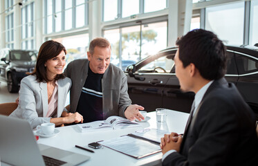 Middle aged caucasian couple talking to a car salesman about purchasing a vehicle in a car dealership