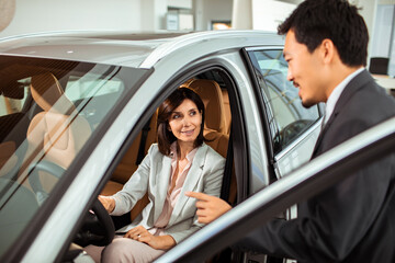 Middle aged caucasian woman testing out a car with the help of a car salesman in a car dealership