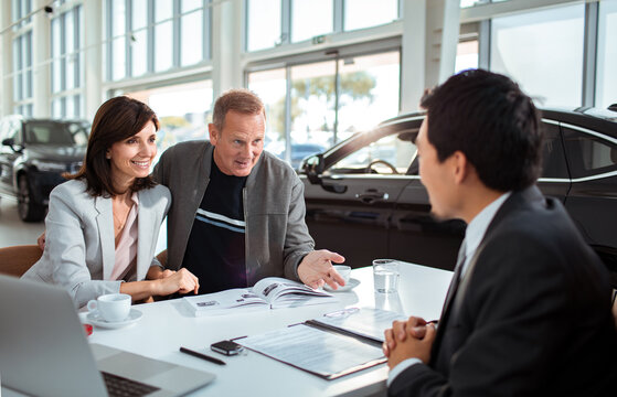 Middle aged caucasian couple talking to a car salesman about purchasing a vehicle in a car dealership