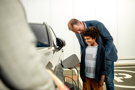 Father and son charging their new electric car at a car dealership with the help of a car salesman