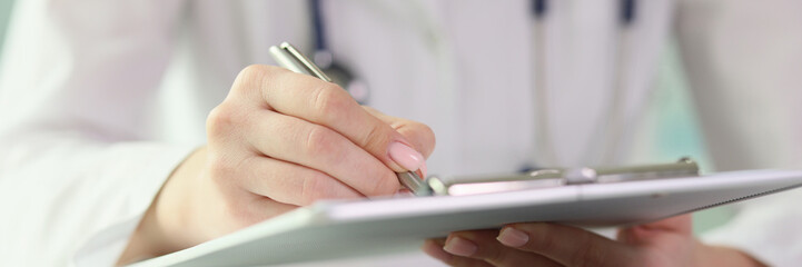 Close-up of female doctor holding clipboard and making notes in medical papers.