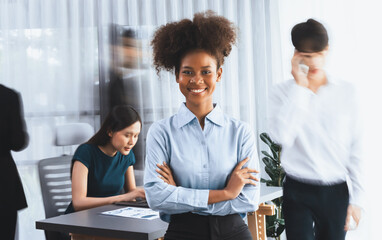 Young African businesswoman portrait poses confidently with diverse coworkers in busy meeting room in motion blurred background. Multicultural team works together for business success. Concord