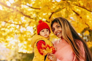A mother and her child play with leaves in the autumn park. Communication and pastime with children.