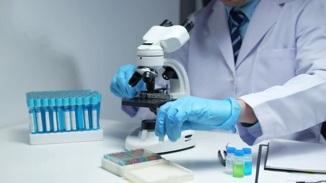 Asian scientist looking at a microscopic sample of experimental cyan is doing an in vitro vaccine experiment in a science lab. medical research concept.