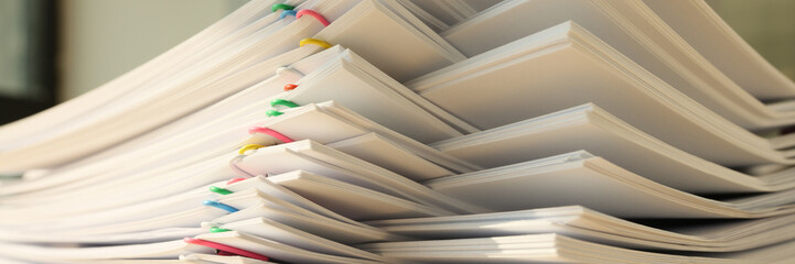 High stack of office documents with clips on office table close up.