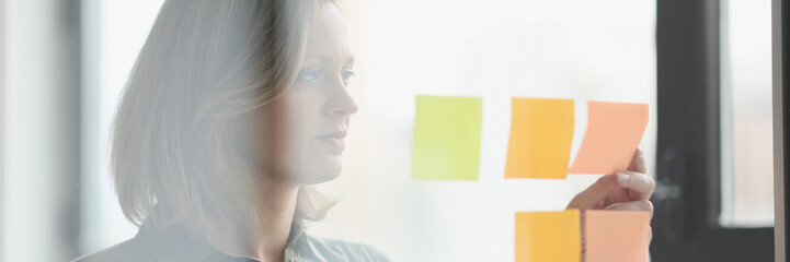 Fototapeta premium Female manager sticks note papers to transparent glass wall in office.