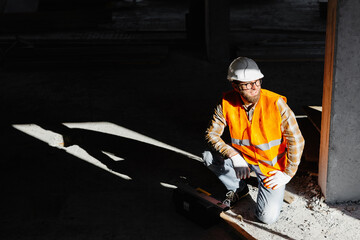 Builder repairman, foreman in safety helmet and vest works at his workplace in a building under construction