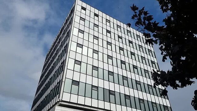 Glass front modern downtown college office building reflecting cloudy blue sky, Slow tilt down