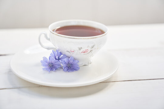 Cichorium flowers in a saucer, on the background of a mug with an invigorating drink. Flowers of ordinary chicory or cichorium dioecious. With space to copy. High quality photo