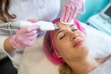 beautician with an ultrasonic scrubber works with the skin of a woman's face.