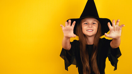Portrait of an angry little girl in a witch costume, on a yellow background. Happy halloween.