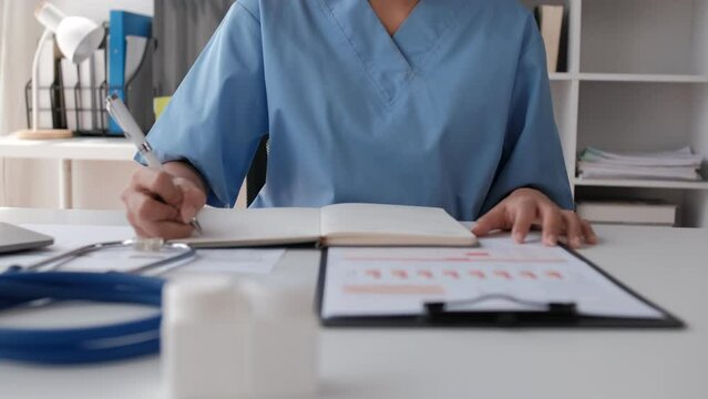 Asian female medical student studies a medical textbook on a laptop computer in a hospital hall.