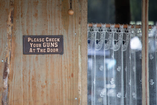 Please Check Your Guns at the Door  panel text metal sign in wooden bar saloon facade entrance means forbidden weapons