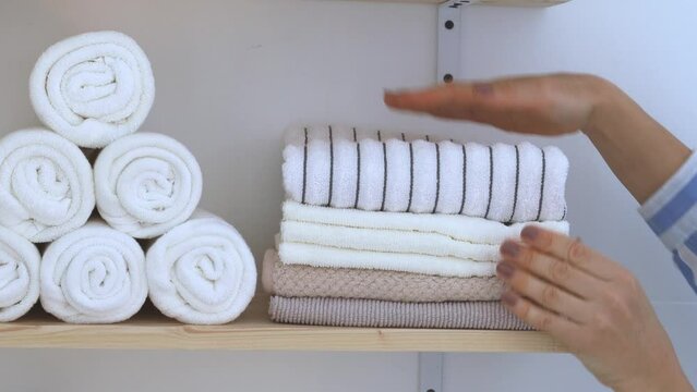 A woman puts clean white towels stacked on a shelf in the bathroom. 