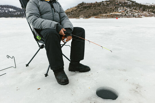 Boy sits on frozen lake fishing in ice hole in winter in coat