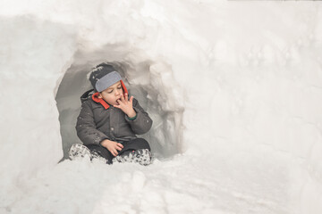 Young boy playing in snow fort on winter day. - obrazy, fototapety, plakaty