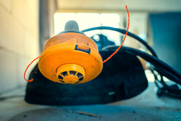 Reel of a gasoline trimmer with fishing line close-up, blurred background. A universal tool for mowing grass on a private plot.