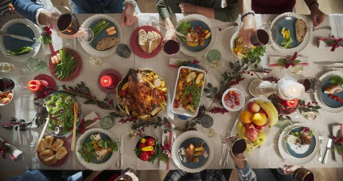 Parents, Children and Friends Enjoying Christmas Dinner Together in a Cozy Home. Relatives Sharing Meals, Raising Glasses with Red Wine, Toasting, Celebrating a Holiday. Top Down View Footage