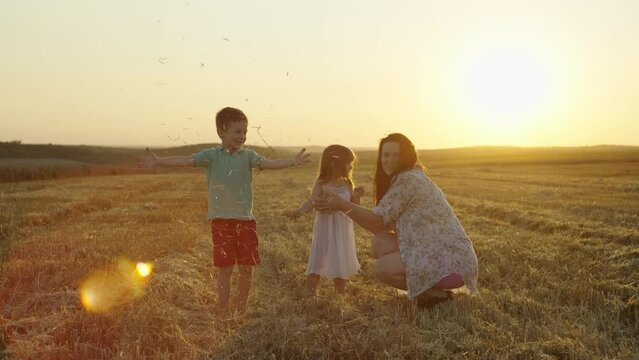 Cheerful children with their mother throw hay uphill, rejoice and laugh. A happy family fools around together on the farm agro field. High quality 4k footage