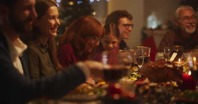 Intimate Family Dinner Setting with a Group of Diverse Relatives Celebrating Christmas, Dining Together at a Big Table in Decorated Living Room. Loved Ones Talking, Laughing and Enjoying Tasty Meals 