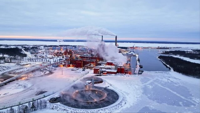 Aerial view in front of the smoking Nuottasaari factory, winter sunset in Oulu