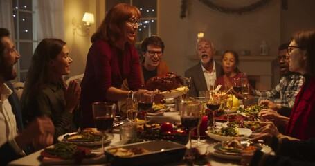 Diverse Group of Relatives and Friends Sitting Together Behind a Dining Table with Tasty Meals and Festive Decorations. Senior Woman Bringing a Turkey Feast, Creating a Joyful Holiday Atmosphere - Powered by Adobe