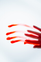 Hand of unrecognizable lady, smeared with red paint, leaving handprint on white background, creating art for Halloween.