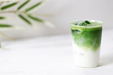 Glass of iced green tea latte on white wooden table.