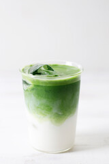Glass of iced green tea latte on white wooden table.