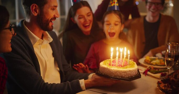 Young Handsome Father Bringing a Birthday Cake with Candlelights to His Cute Daughter. Excited Girl Blowing Out Candles and Making a Wish at a Family Dinner Celebration at Home