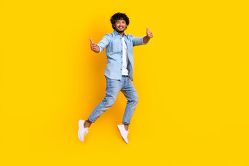 Fototapeta na wymiar Full length photo of funky cool man wear jeans shirt jumping high thumbs up empty space isolated yellow color background