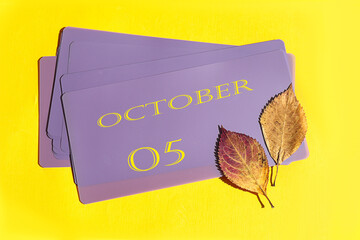 Calendar for October 5: name of the month October in English, numbers 05, autumn leaves on a yellow-violet background, top view