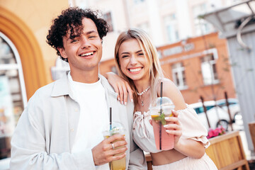Fototapeta na wymiar Young smiling beautiful woman and her handsome boyfriend in casual summer clothes. Happy cheerful family. Female having fun. Couple posing in street. Holding and drinking cocktail drink in plastic cup