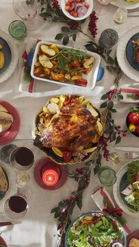 Vertical Screen: Tastefully Decorated Christmas Banquet Table with a Roast Turkey, Vegetables, Baked Potatoes, Desserts. Top Down View Footage with People Putting Dishes on a Dining Table at Home
