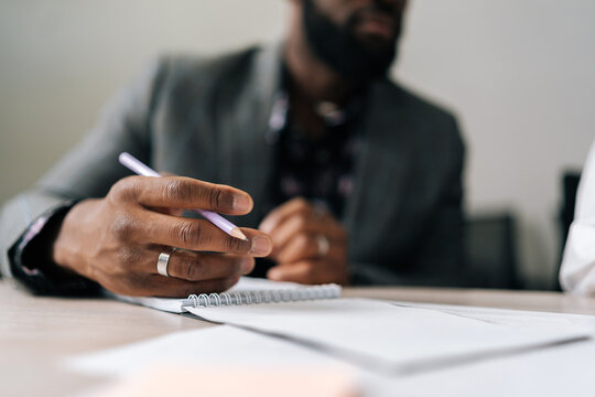 Close-up Cropped Shot Of Unrecognizable Black Businessman In Suit Sitting At Office Table And Holding Pen. Makes Appointment Notes Time, Writes Important Things And To-do List Not To Forget