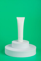 Plastic white tube for cream or lotion. Skin care or sunscreen cosmetic with stylish props on green background 