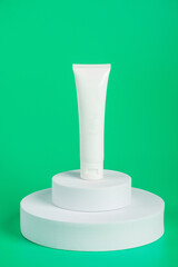 Plastic white tube for cream or lotion. Skin care or sunscreen cosmetic with stylish props on green background 